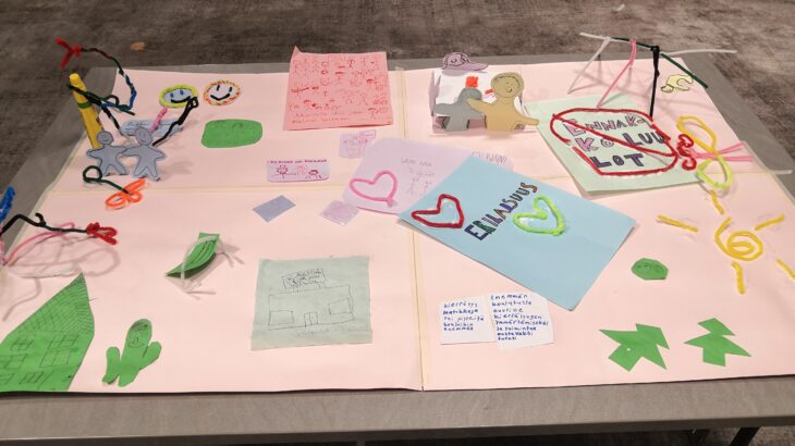 Askartelutyö isolla paperilla, johon kuvattuna muun muassa kädestä toisiaan pitävät hahmot, kuva lapsista erilaisissa harrastuksissa, perhe pöydän ympärillä, kauppa, talo, aurinko ja puita. Työhön kirjoitetuissa teksteissä muun muassa: erilaisuus on rikkaus, erilaisuus ja sydämiä, kieltomerkki ennakkoluuloille.