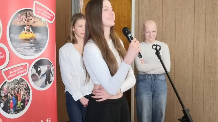 Kolme nuorta pitää puhetta mikrofonin ääressä Nuorten Kotkien rollupin edessä